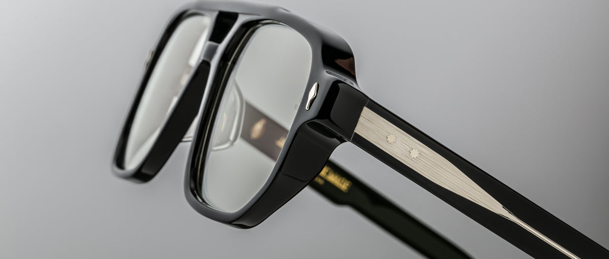 Close-up of Jacques Marie Mage Evans optical glasses, featuring a black and silver oversized acetate frame with clear lenses and detailed temple hinges, set against a neutral background.