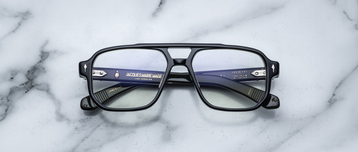 The Jacques Marie Mage Evans handcrafted black rectangular optical glasses with clear lenses rest on a white marble surface, highlighting the brand’s details in the oversized acetate frame.