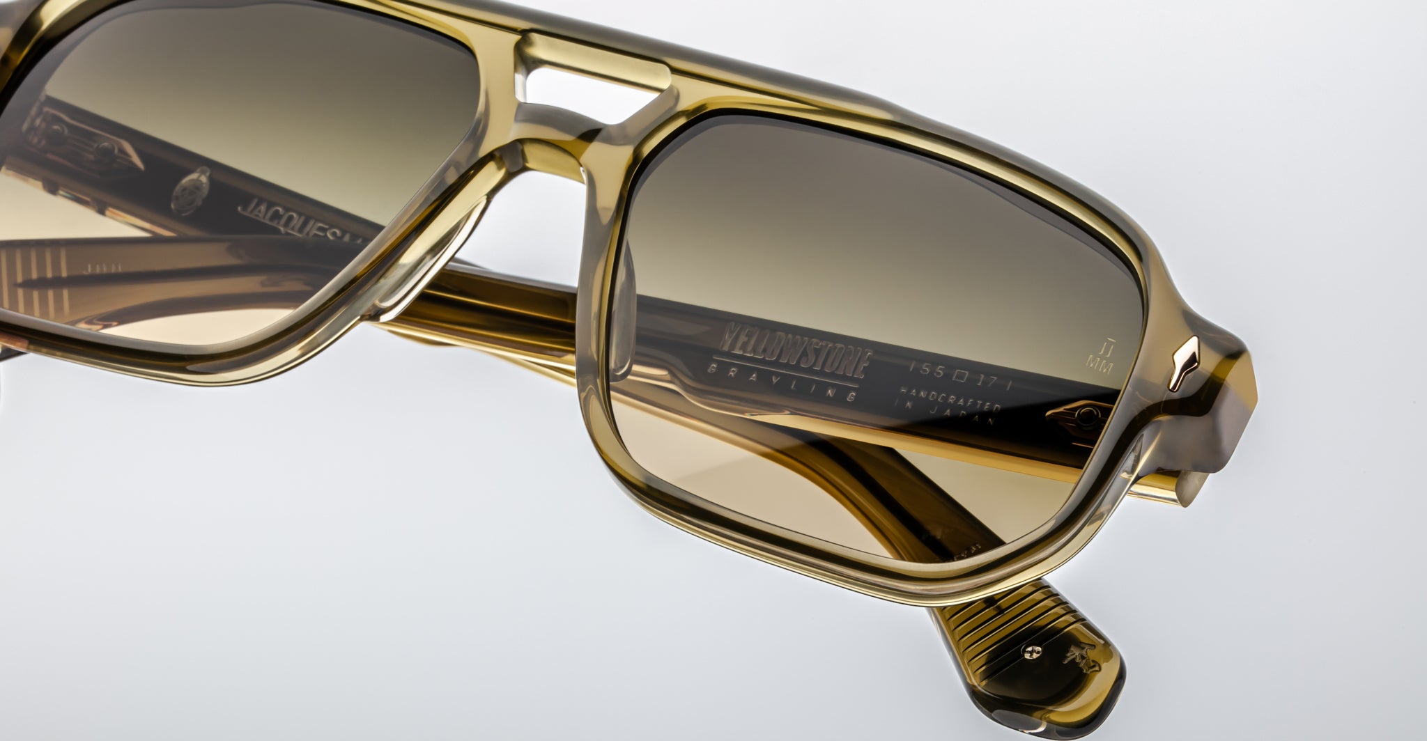 Close-up of Jacques Marie Mage Evans sunglasses in brown acetate with tinted lenses, showcasing oversized rectangular frames and signature branded temple details, all handcrafted by Jacques Marie Mage against a white background.