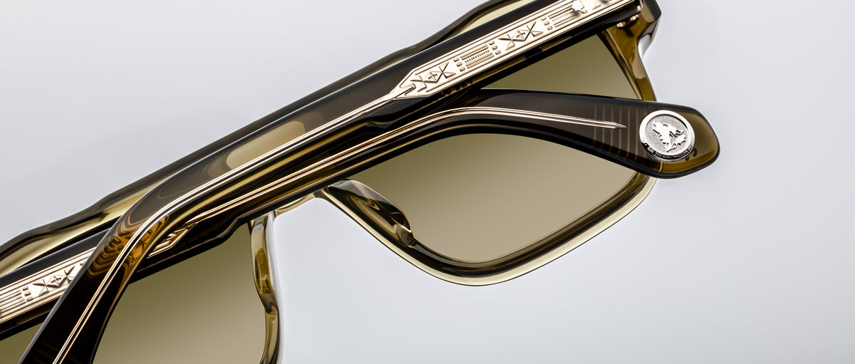 A close-up of two pairs of Jacques Marie Mage Evans sunglasses, featuring engraved metal detailing on the oversized acetate frame and a signature round medallion on the temple.