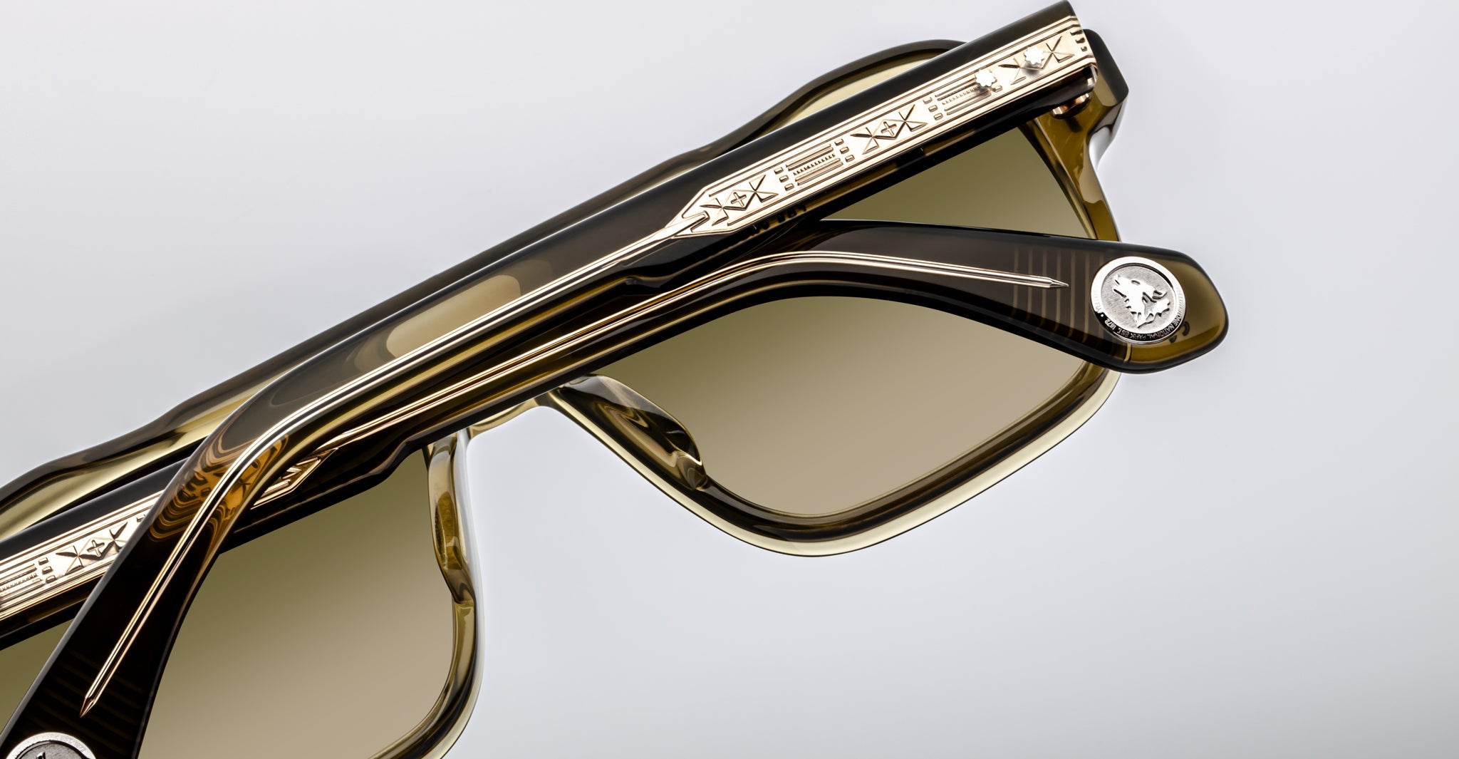 A close-up of two pairs of Jacques Marie Mage Evans sunglasses, featuring engraved metal detailing on the oversized acetate frame and a signature round medallion on the temple.