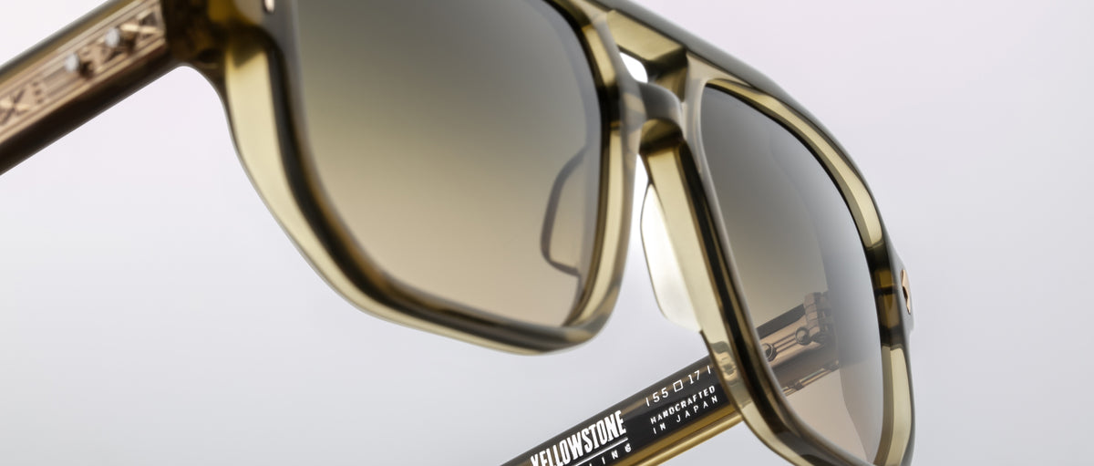 Close-up of Jacques Marie Mage Evans sunglasses featuring a thick, oversized acetate frame with brown-tinted lenses. The distinctive branding and model details on the arm highlight Jacques Marie Mage's signature handcrafted style.