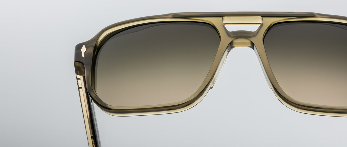 Close-up of Jacques Marie Mage Evans sunglasses featuring an oversized acetate frame in translucent khaki with brown gradient lenses, set against a plain light background.