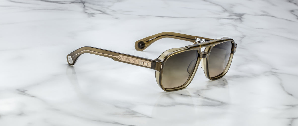 The Jacques Marie Mage Evans sunglasses, featuring oversized rectangular acetate frames in a brown tint, rest on a white marble surface.