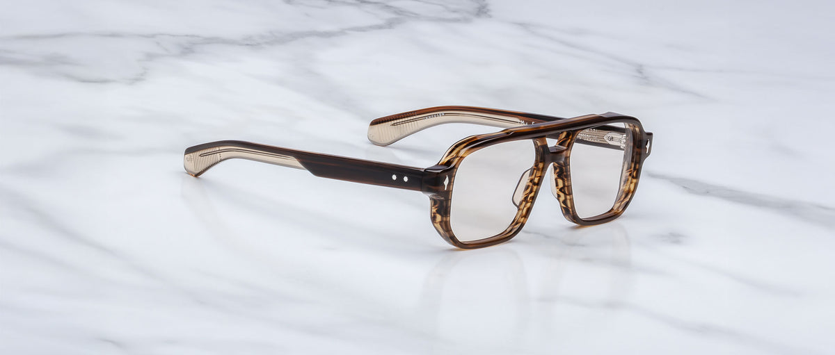 A pair of Jacques Marie Mage Evans brown tortoiseshell rectangular eyeglasses with clear lenses and an oversized acetate frame rests on a white marble surface.
