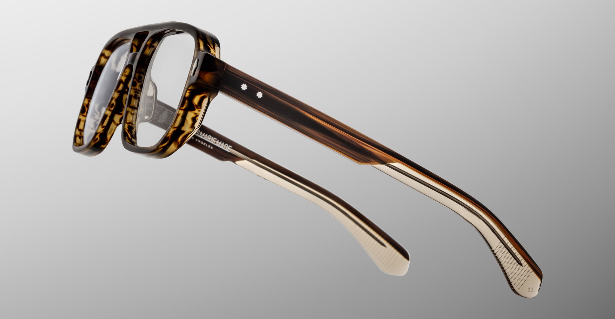 Close-up of Jacques Marie Mage Evans optical glasses, featuring oversized brown tortoiseshell acetate frames and clear lenses, displayed at an angle on a light gray background.