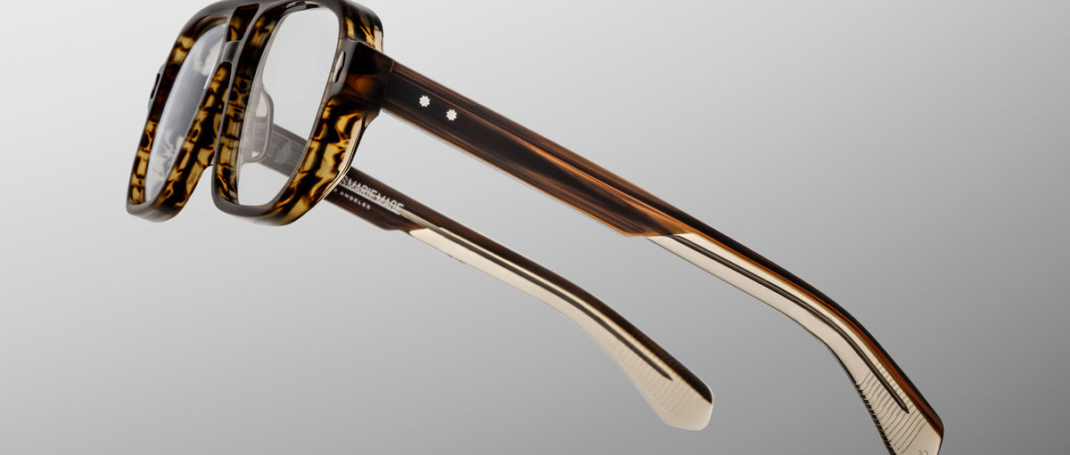 Close-up of Jacques Marie Mage Evans optical glasses, featuring oversized brown tortoiseshell acetate frames and clear lenses, displayed at an angle on a light gray background.