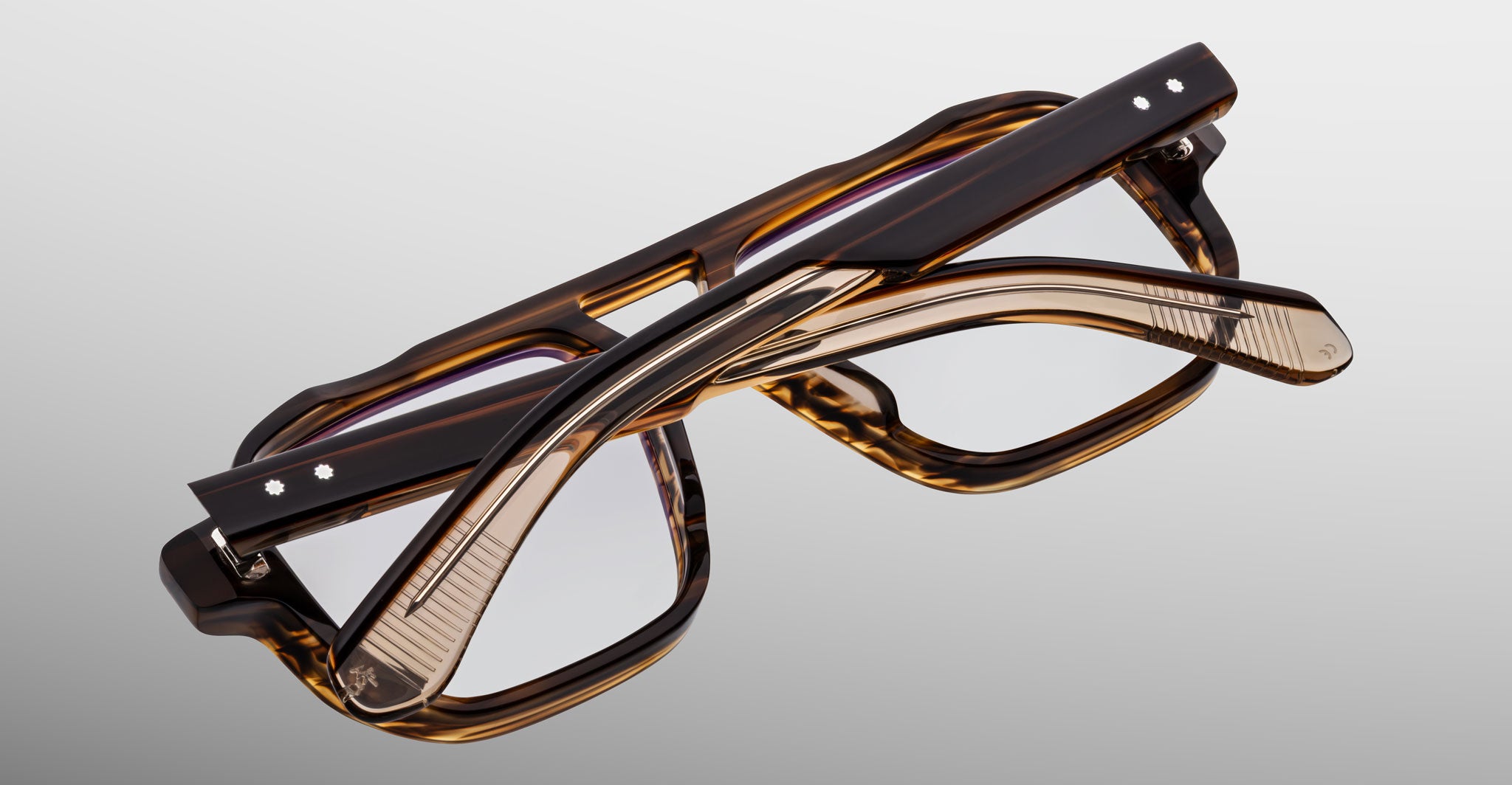 Two pairs of Jacques Marie Mage Evans handcrafted optical glasses with rectangular tortoiseshell frames, including an oversized acetate style, are stacked and interlocked on a plain light gray background.