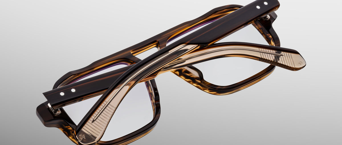 Two pairs of Jacques Marie Mage Evans handcrafted optical glasses with rectangular tortoiseshell frames, including an oversized acetate style, are stacked and interlocked on a plain light gray background.