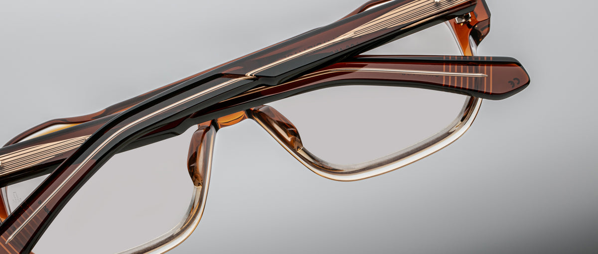Close-up of two handcrafted Jacques Marie Mage Evans optical glasses with oversized brown acetate frames, stacked against a neutral background.