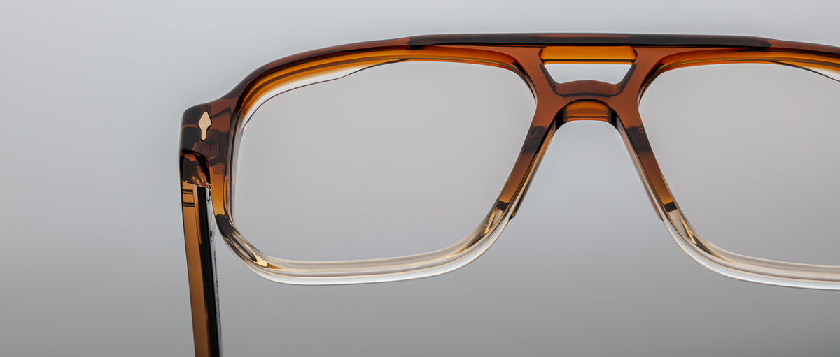 Close-up of the upper half of Jacques Marie Mage Evans optical glasses by Jacques Marie Mage, featuring rectangular frames in brown and clear acetate, set against a plain gray background.