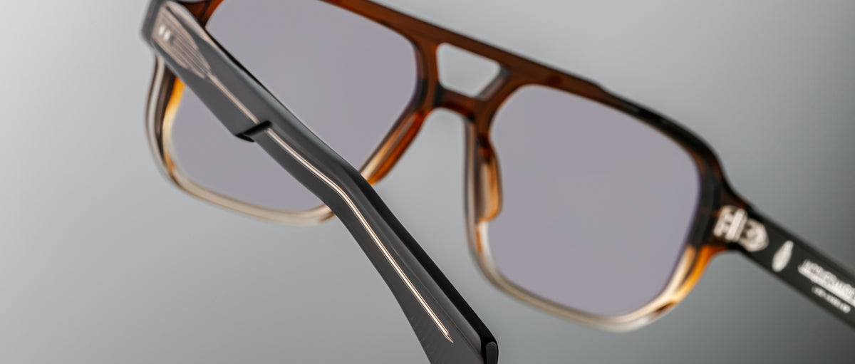 Close-up of Jacques Marie Mage Evans handcrafted brown optical glasses with gray tinted lenses, showcasing detailed black arm accents against a neutral background.