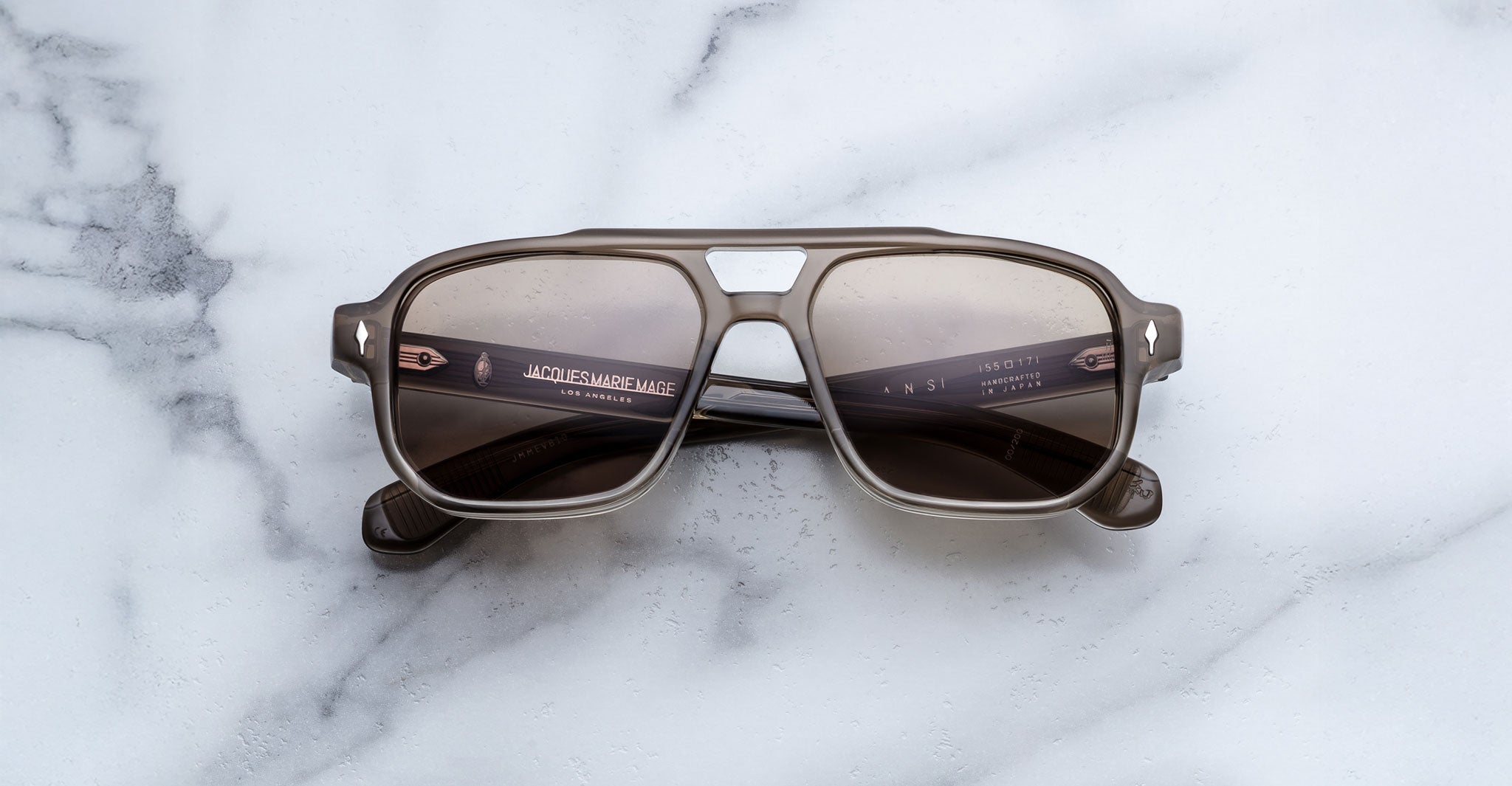 The Jacques Marie Mage Evans sunglasses by Jacques Marie Mage feature an oversized brown acetate square frame with dark lenses, displayed on a white marble surface.