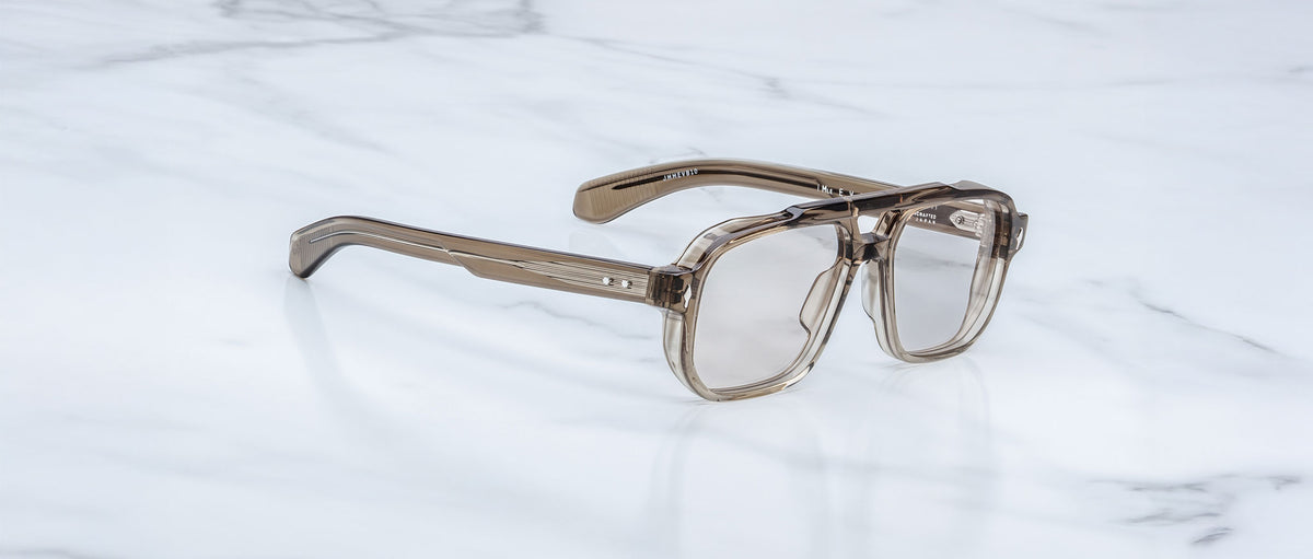 Jacques Marie Mage Evans optical glasses with a translucent brown oversized acetate frame, handcrafted and inspired by the brand’s signature style, displayed on a white marble surface.