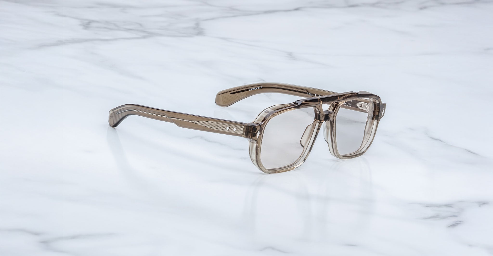 Jacques Marie Mage Evans optical glasses with a translucent brown oversized acetate frame, handcrafted and inspired by the brand’s signature style, displayed on a white marble surface.
