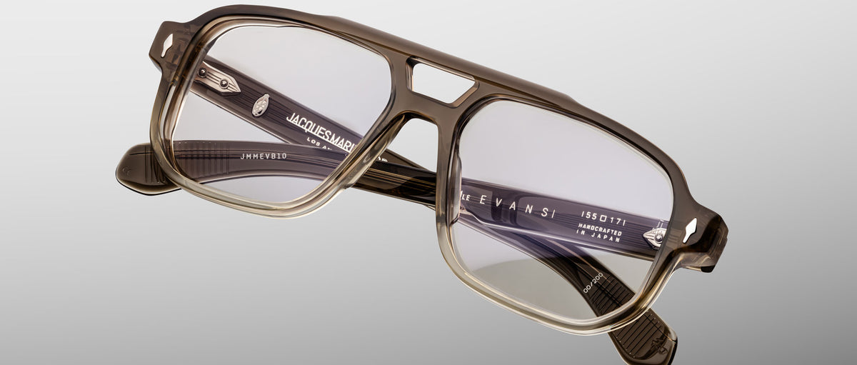 A pair of Jacques Marie Mage Evans eyeglasses featuring an oversized rectangular translucent brown acetate frame with clear lenses, shown on a light gray background.