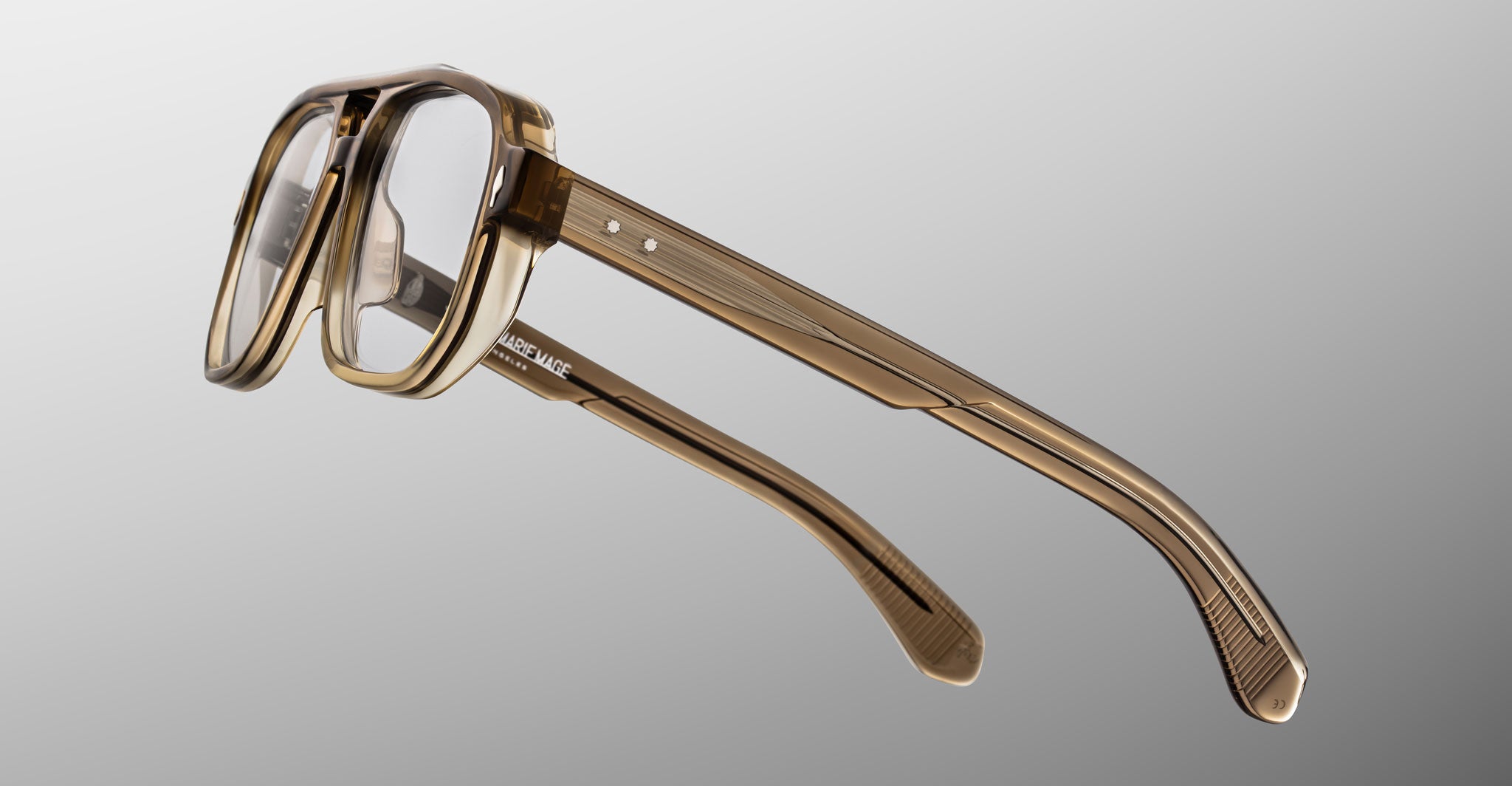 The Jacques Marie Mage Evans glasses showcase an oversized brown translucent rectangular acetate frame, displayed at an angle on a plain gray background.