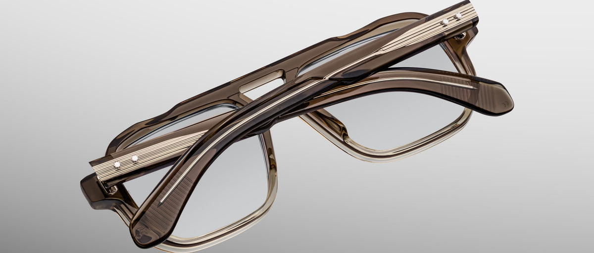 Two pairs of Jacques Marie Mage Evans handcrafted optical glasses with brown oversized acetate frames are stacked against a gradient gray background, showcasing a refined Jacques Marie Mage aesthetic.