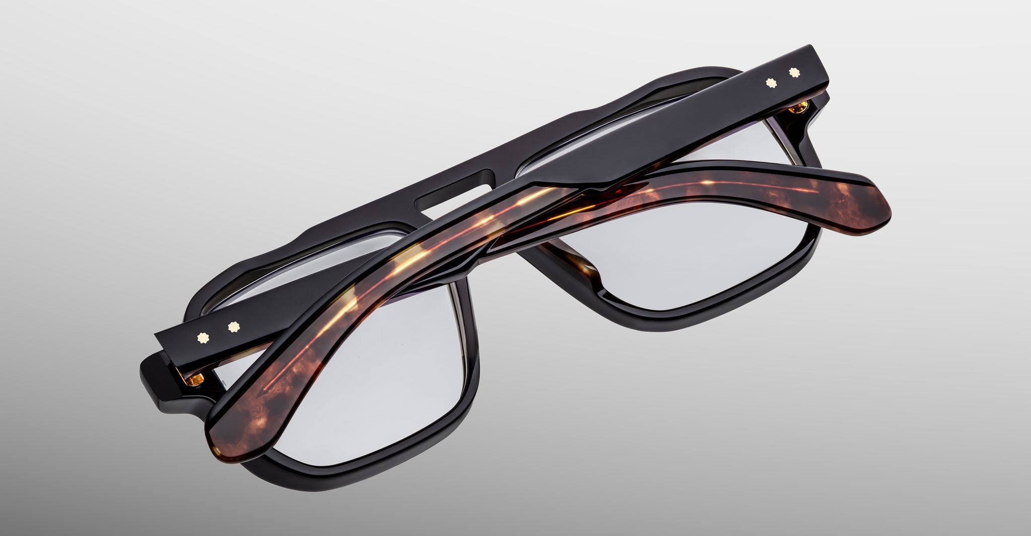 Two pairs of Jacques Marie Mage Evans handcrafted optical glasses—one with oversized black acetate frames, the other in tortoiseshell—are stacked against a neutral background, capturing the signature style of Jacques Marie Mage.