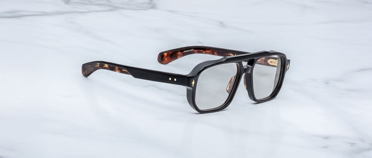 The Jacques Marie Mage Evans optical glasses, featuring an oversized brown tortoiseshell acetate frame, are elegantly displayed on a white marble surface.