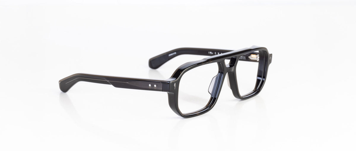 The Jacques Marie Mage Evans are black rectangular eyeglasses with a thick, oversized handcrafted acetate frame by Jacques Marie Mage, elegantly displayed on a white surface.