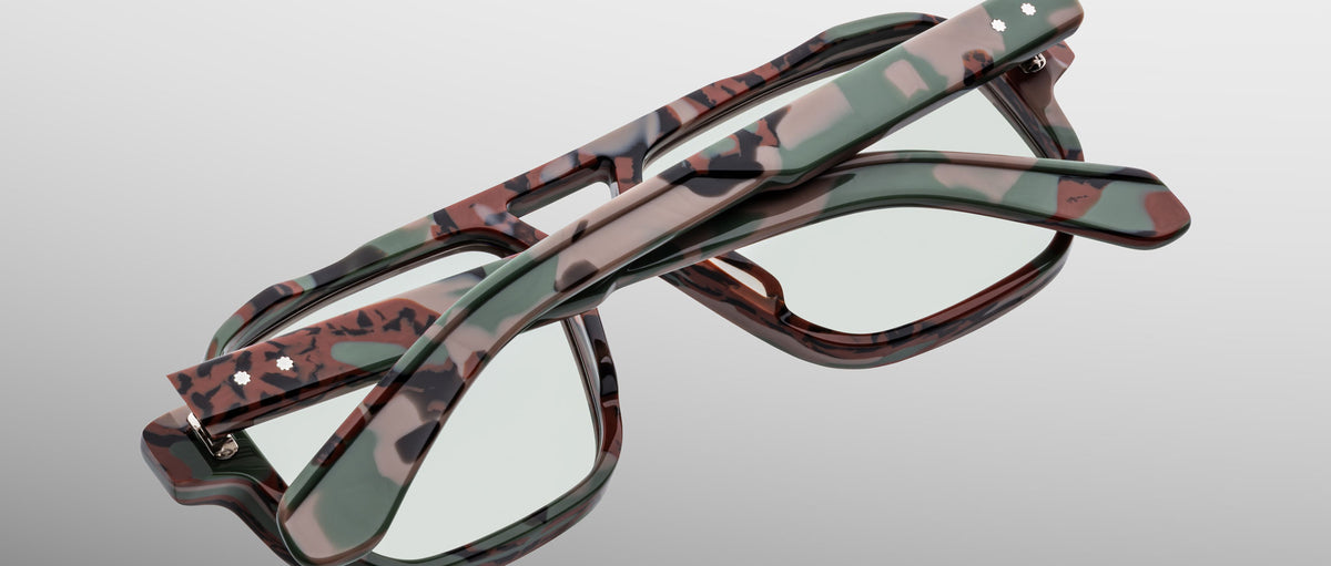 Two pairs of Jacques Marie Mage Evans optical glasses, featuring handcrafted oversized acetate frames, are stacked in a crisscross arrangement on a light grey background.