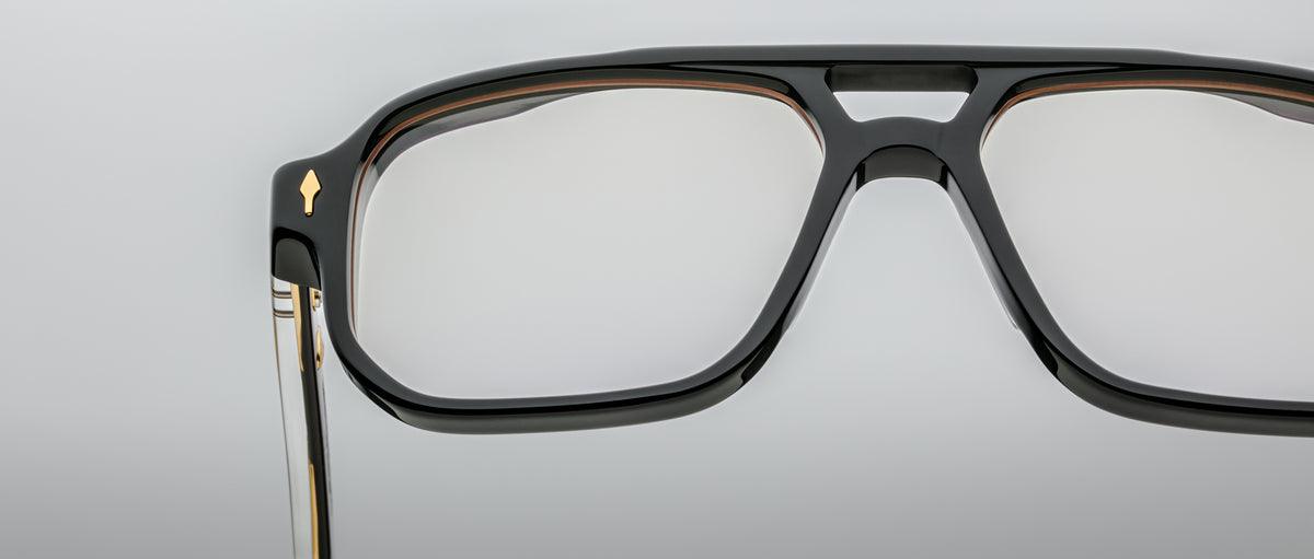 Close-up of the Jacques Marie Mage Evans black rectangular eyeglass frames, featuring a metal detail on the temple and oversized acetate design, shown against a plain light background.
