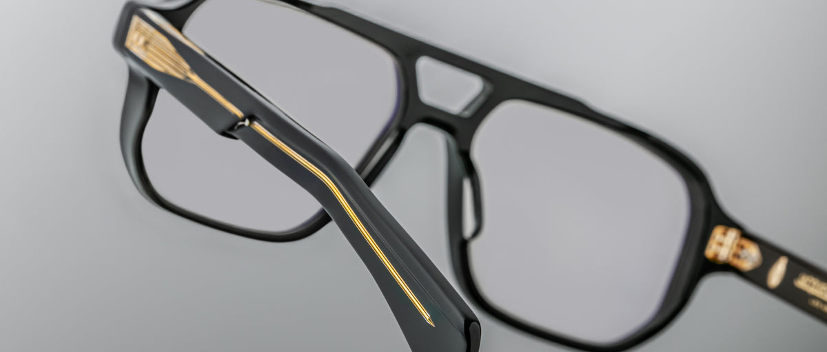 Close-up of the Jacques Marie Mage Evans optical glasses, featuring black oversized acetate frames with gold detailing on the arms and hinges, set against a neutral background.