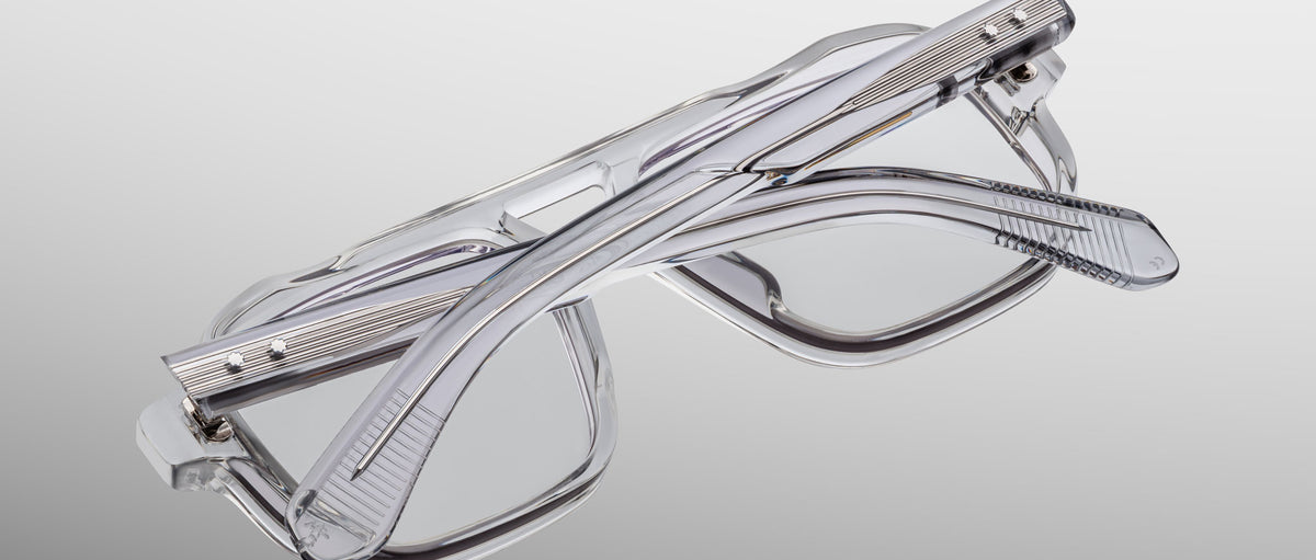 The Jacques Marie Mage Evans, a pair of handcrafted rectangular optical glasses by Jacques Marie Mage, is folded and set on a light gray gradient background.