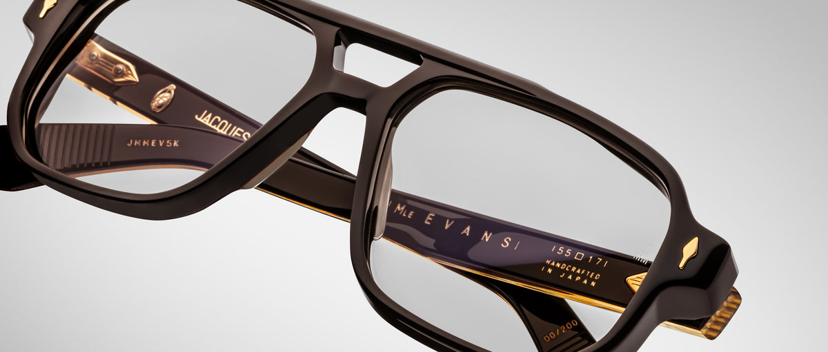 Close-up of Jacques Marie Mage Evans optical glasses, handcrafted with a black and gold oversized acetate frame featuring intricate design details and embossed inner arm text.