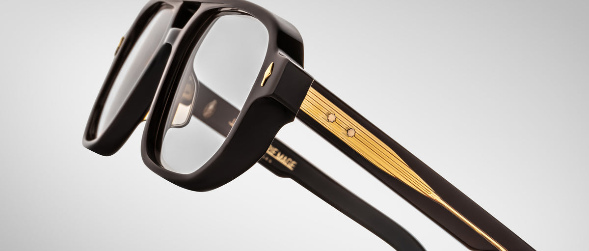 Close-up of Jacques Marie Mage Evans glasses, showcasing oversized black acetate frames, clear lenses, and gold temple detailing by Jacques Marie Mage, set against a plain light background.