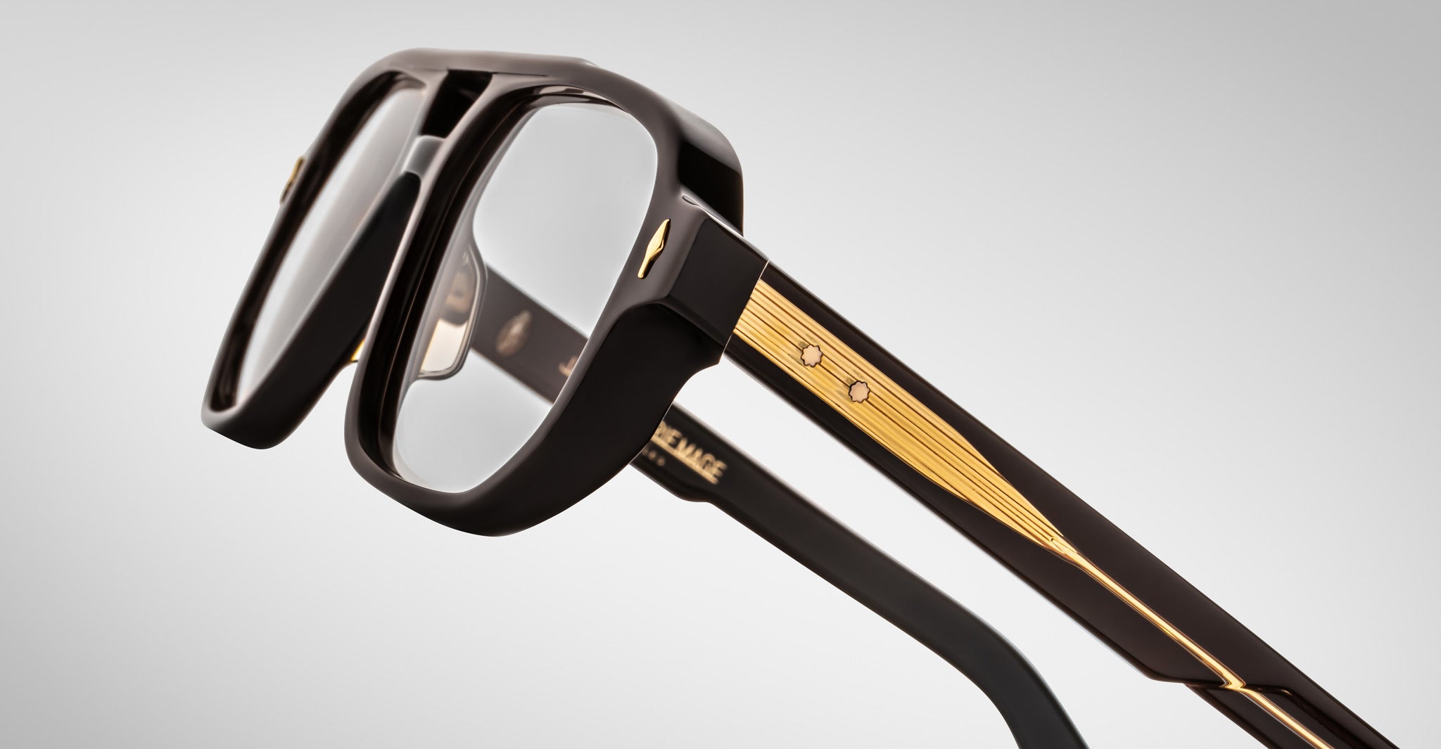 Close-up of Jacques Marie Mage Evans glasses, showcasing oversized black acetate frames, clear lenses, and gold temple detailing by Jacques Marie Mage, set against a plain light background.