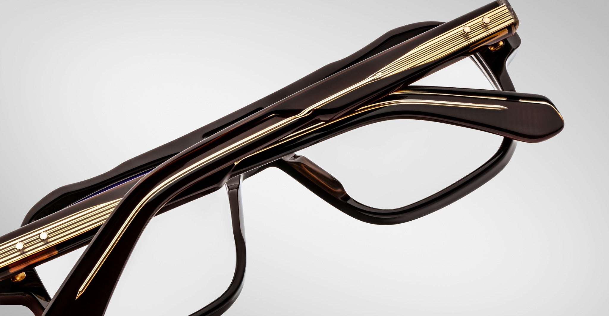 Close-up of folded Jacques Marie Mage Evans eyeglasses featuring black and gold oversized acetate frames, viewed from the side against a plain light background.