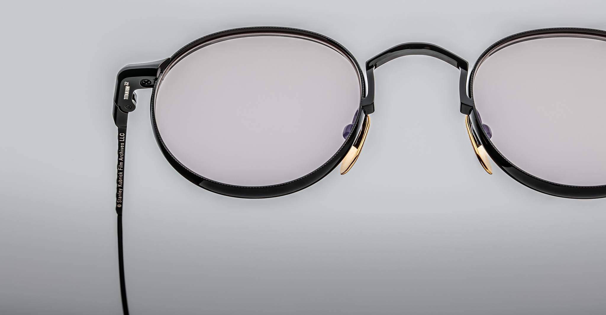 Close-up of Jacques Marie Mage Full Metal Jacket eyeglasses—black round frames with gold accents—set against a plain light gray background.