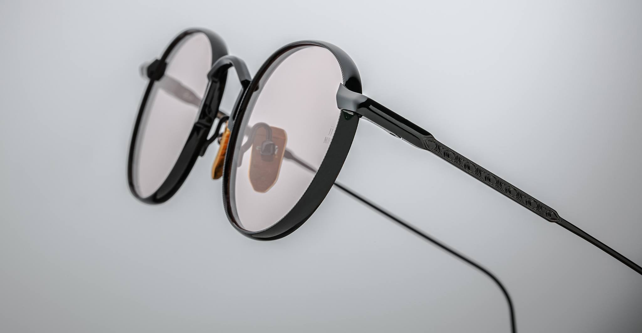 Close-up of Jacques Marie Mage Full Metal Jacket: round, black-rimmed eyeglasses with thin metal arms and light-tinted lenses, set against a plain, light background.