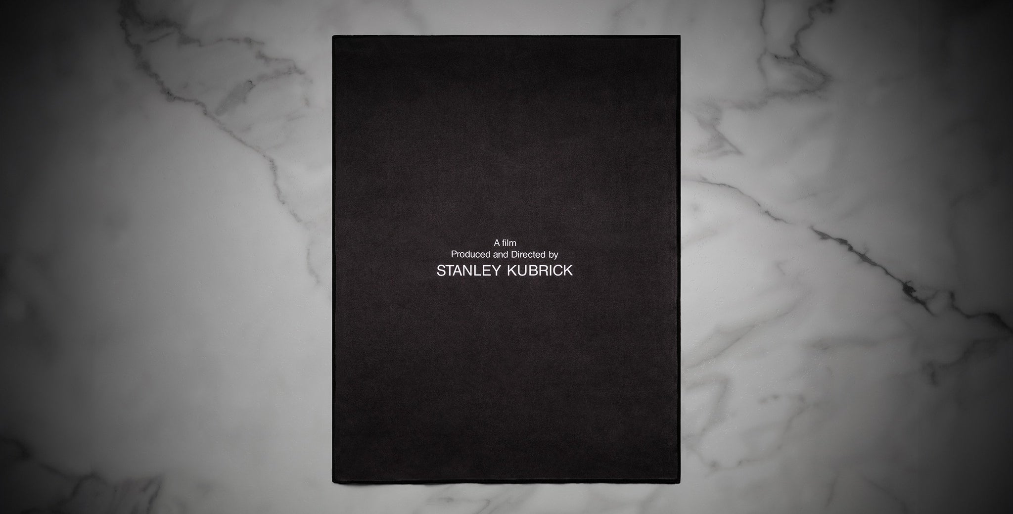 Cleaning cloth, reverse side, with lettering that says, film Produced and Directed by STANLEY KUBRICK, white text on burgundy. The cloth sits on a white marble surface.