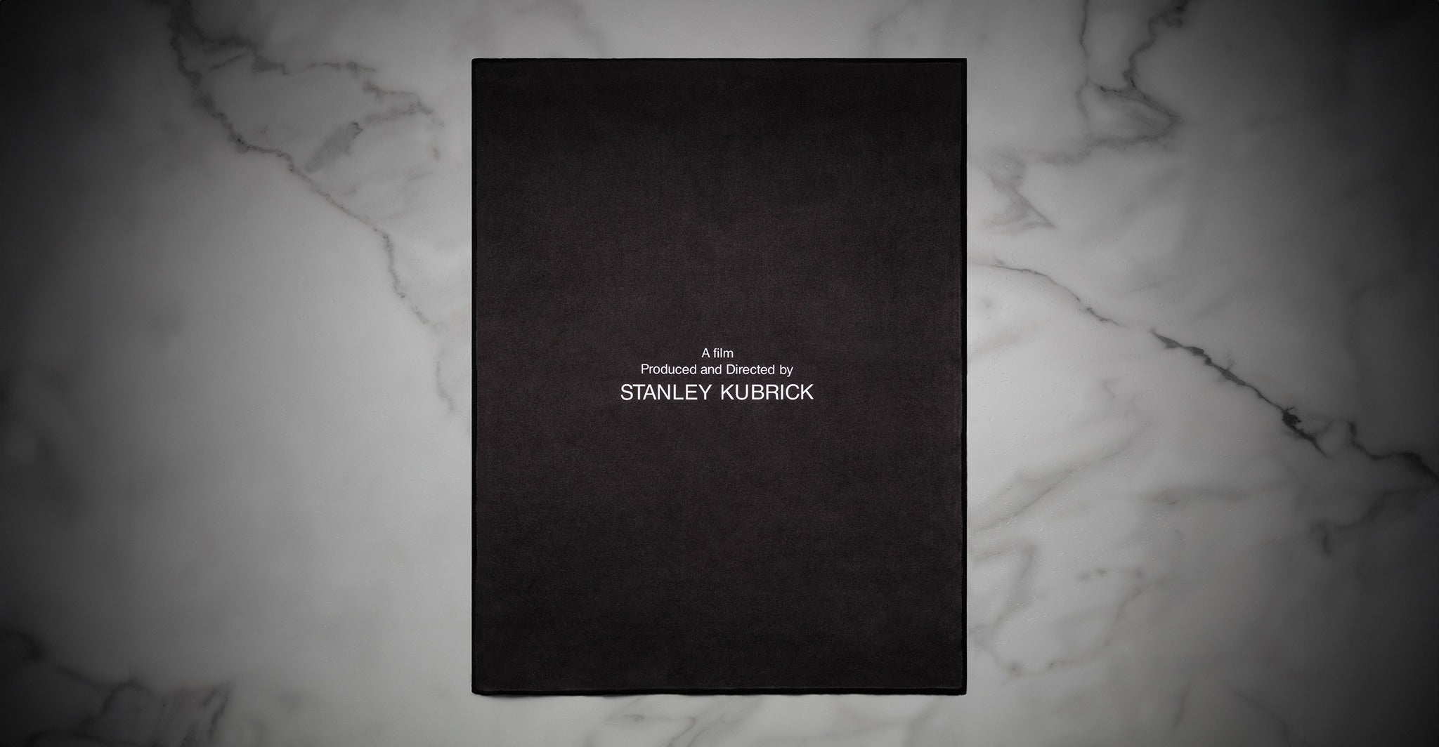Cleaning cloth, reverse side, with lettering that says, film Produced and Directed by STANLEY KUBRICK, white text on burgundy. The cloth sits on a white marble surface.