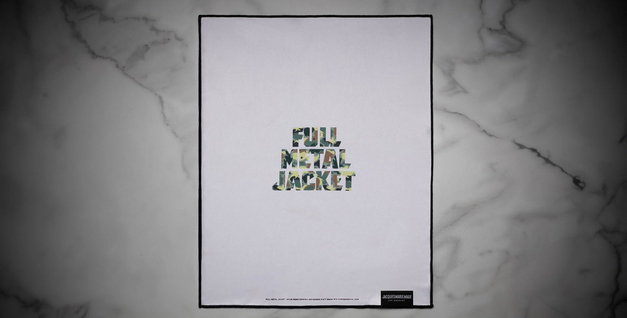 A Jacques Marie Mage Full Metal Jacket poster featuring camouflage-patterned lettering with the words Full Metal Jacket on a white background, displayed on a gray marble surface.