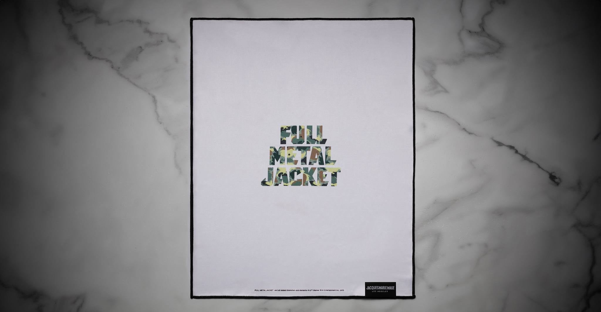 A Jacques Marie Mage Full Metal Jacket poster featuring camouflage-patterned lettering with the words Full Metal Jacket on a white background, displayed on a gray marble surface.