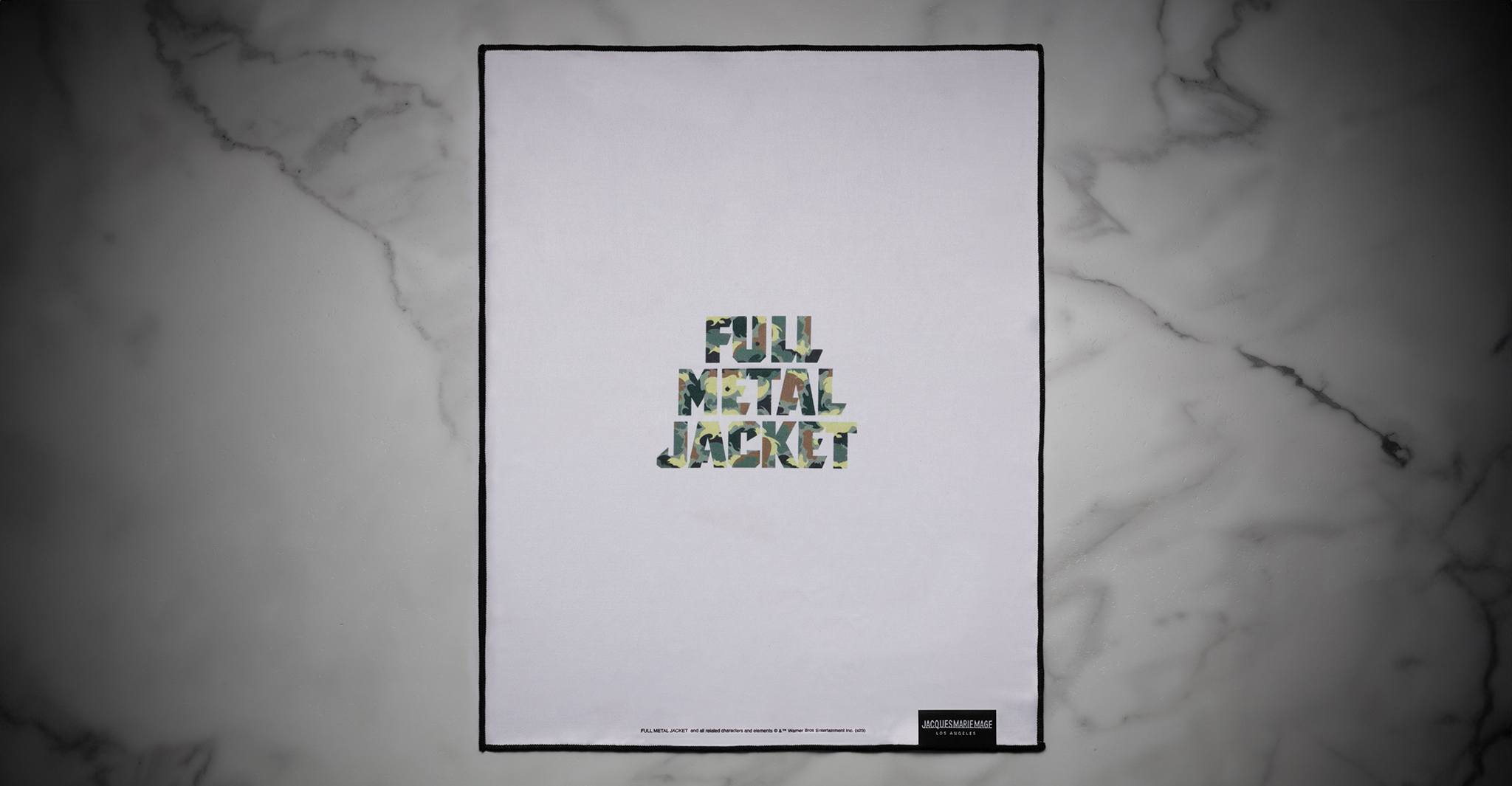 A Jacques Marie Mage Full Metal Jacket poster featuring camouflage-patterned lettering with the words Full Metal Jacket on a white background, displayed on a gray marble surface.