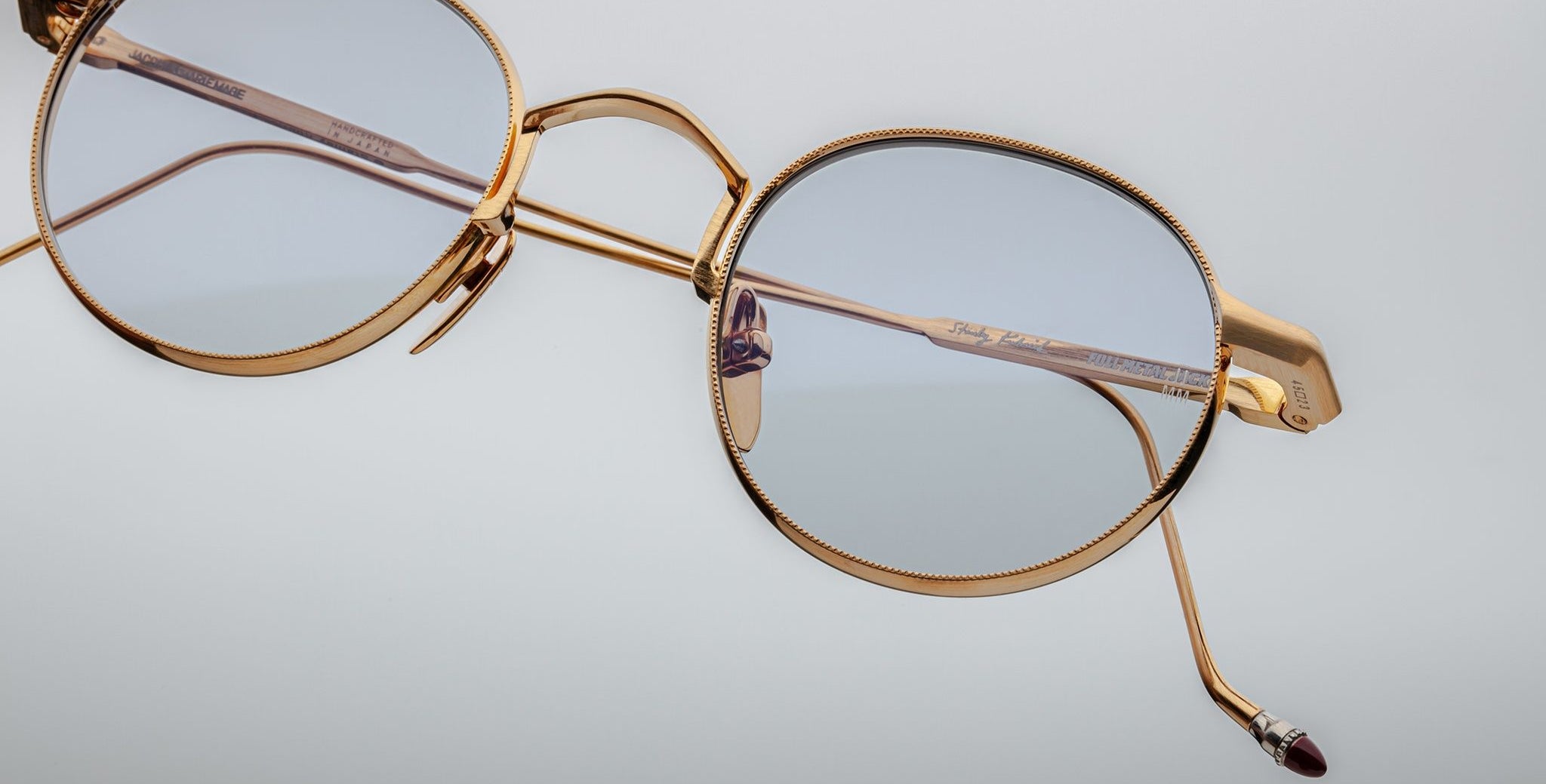 Close-up of Jacques Marie Mage Full Metal Jacket eyeglasses: gold metal frame, light blue round lenses from an angle