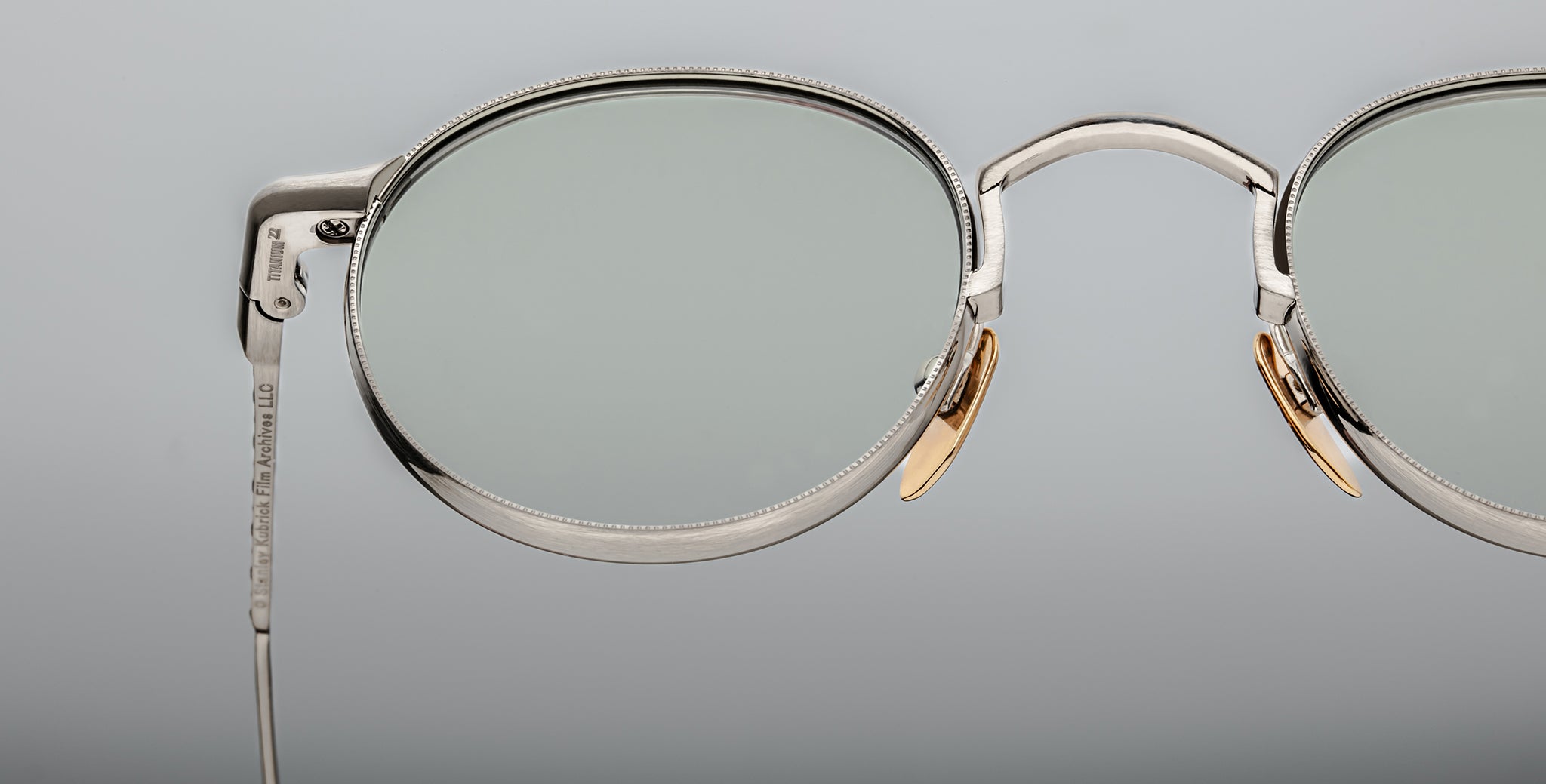 Close-up of Jacques Marie Mage Full Metal Jacket eyeglasses featuring silver oval thin metal frames, clear lenses, and gold nose pads set against a plain, light gray background.