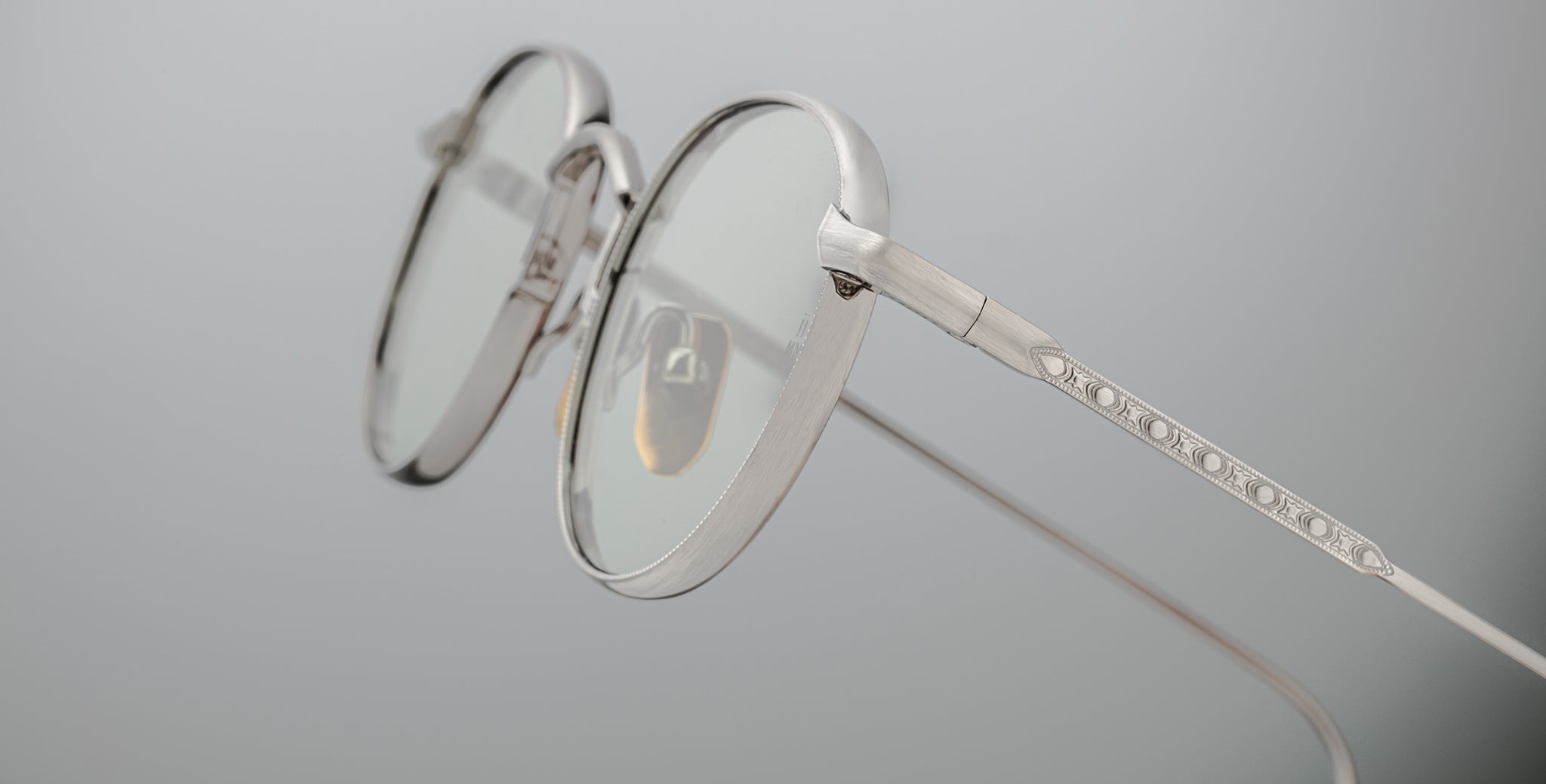 Close-up of Jacques Marie Mage Full Metal Jacket round, silver-framed eyeglasses with clear lenses against a plain light grey background, highlighting the intricate metalwork along the temple arm.