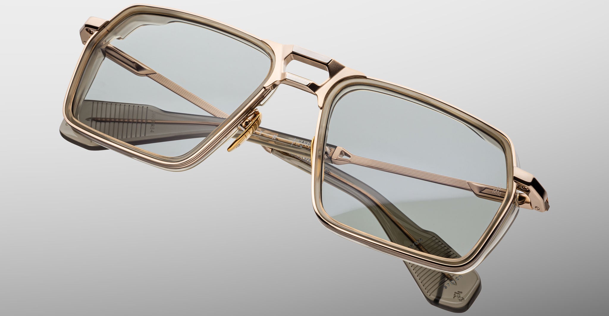 The Jacques Marie Mage GT-R features rectangular gold metal frames and light gray tinted lenses, shown angled against a matching light gray background.