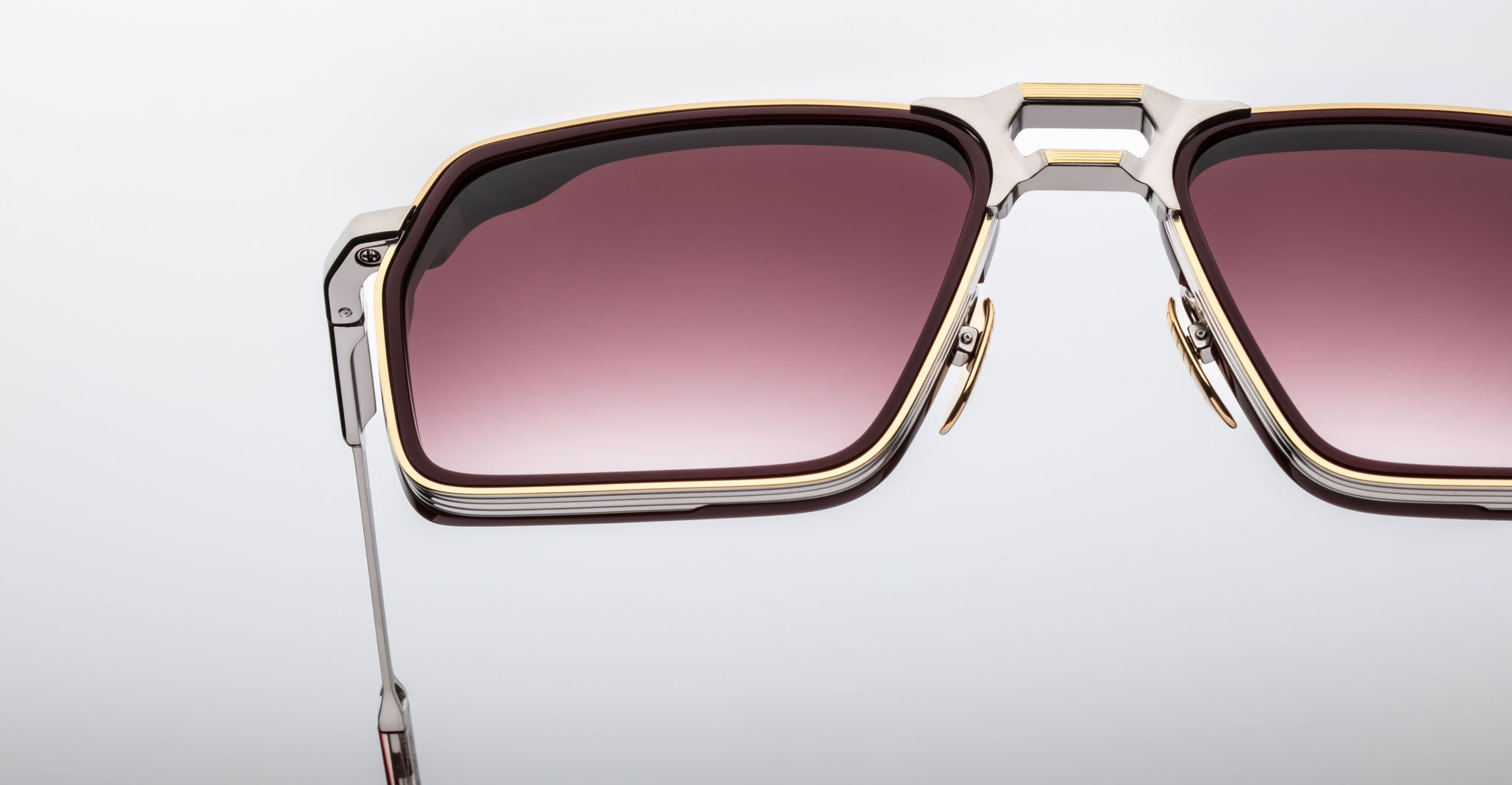 Close-up of the top half of Jacques Marie Mage GT-R rectangular sunglasses with gradient pink lenses, metal frames featuring gold and silver detailing, and visible nose pads, set against a plain light background.