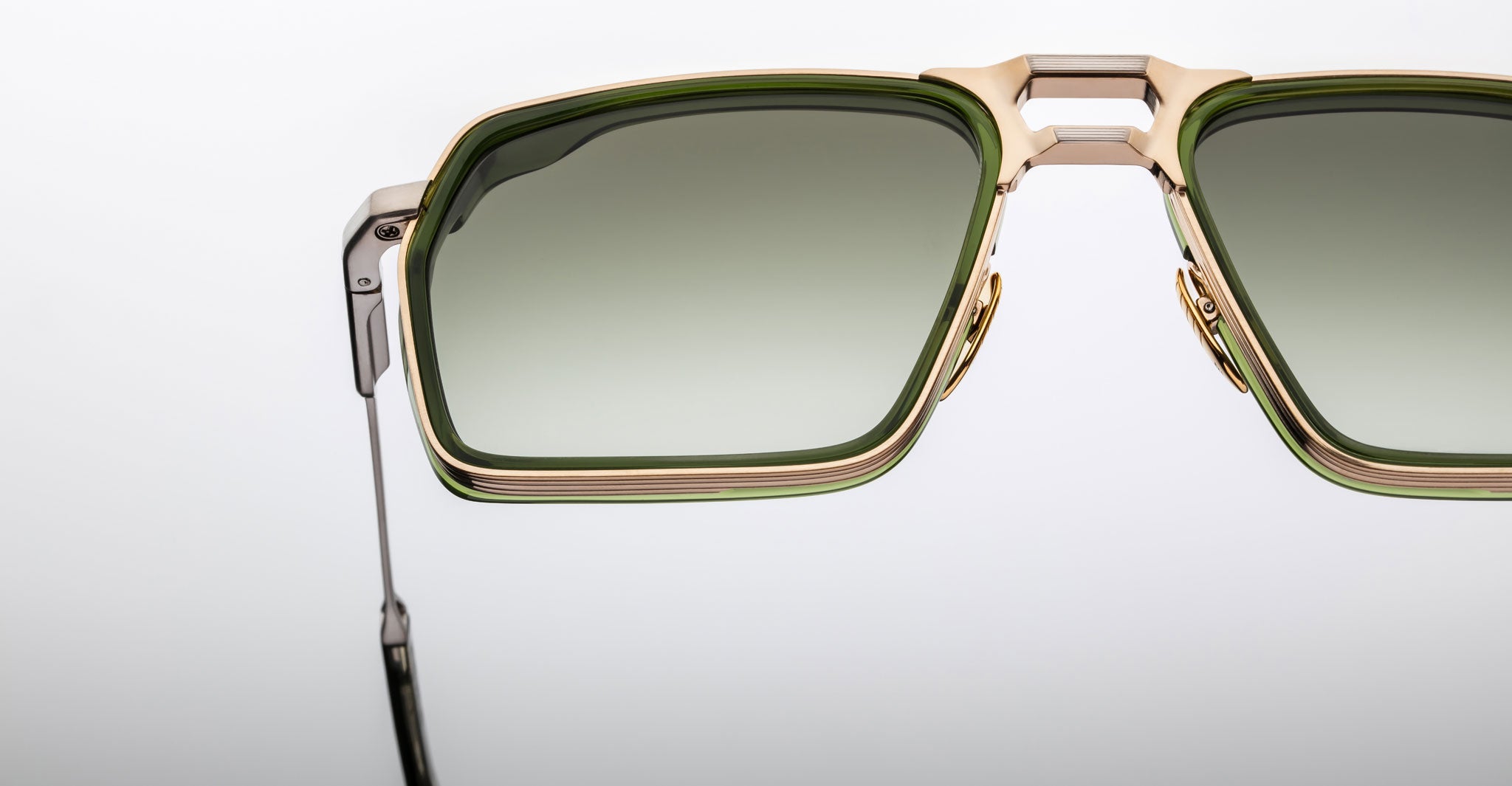 Close-up of Jacques Marie Mage GT-R sunglasses featuring large rectangular green-tinted lenses and a metallic gold and silver frame, photographed against a plain light background.