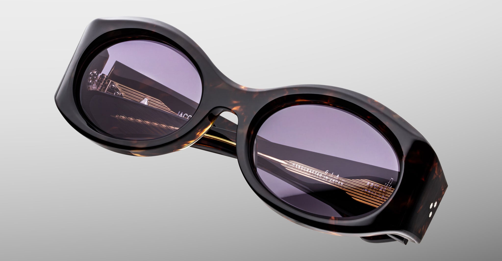Close-up of Jacques Marie Mage Gia in Beau sunglasses with thick tortoiseshell frames and purple-tinted lenses, front view.