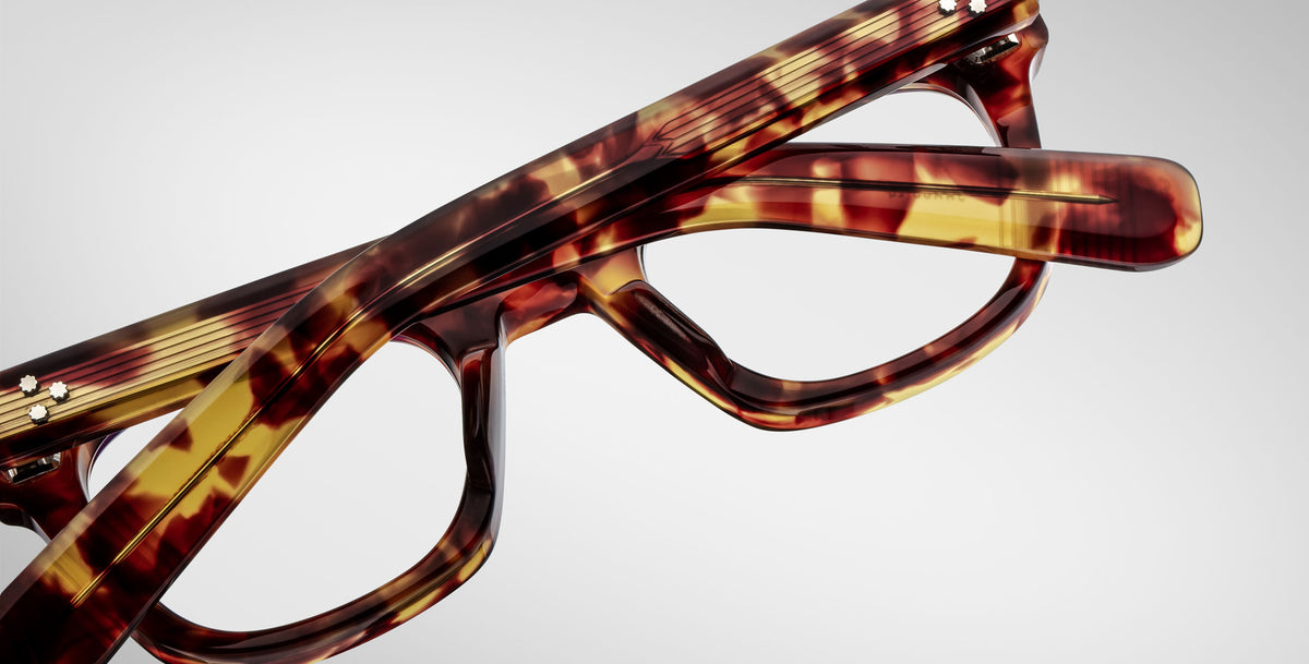 Close-up of two pairs of Jacques Marie Mage Godard tortoiseshell eyeglasses stacked together on a plain white background.