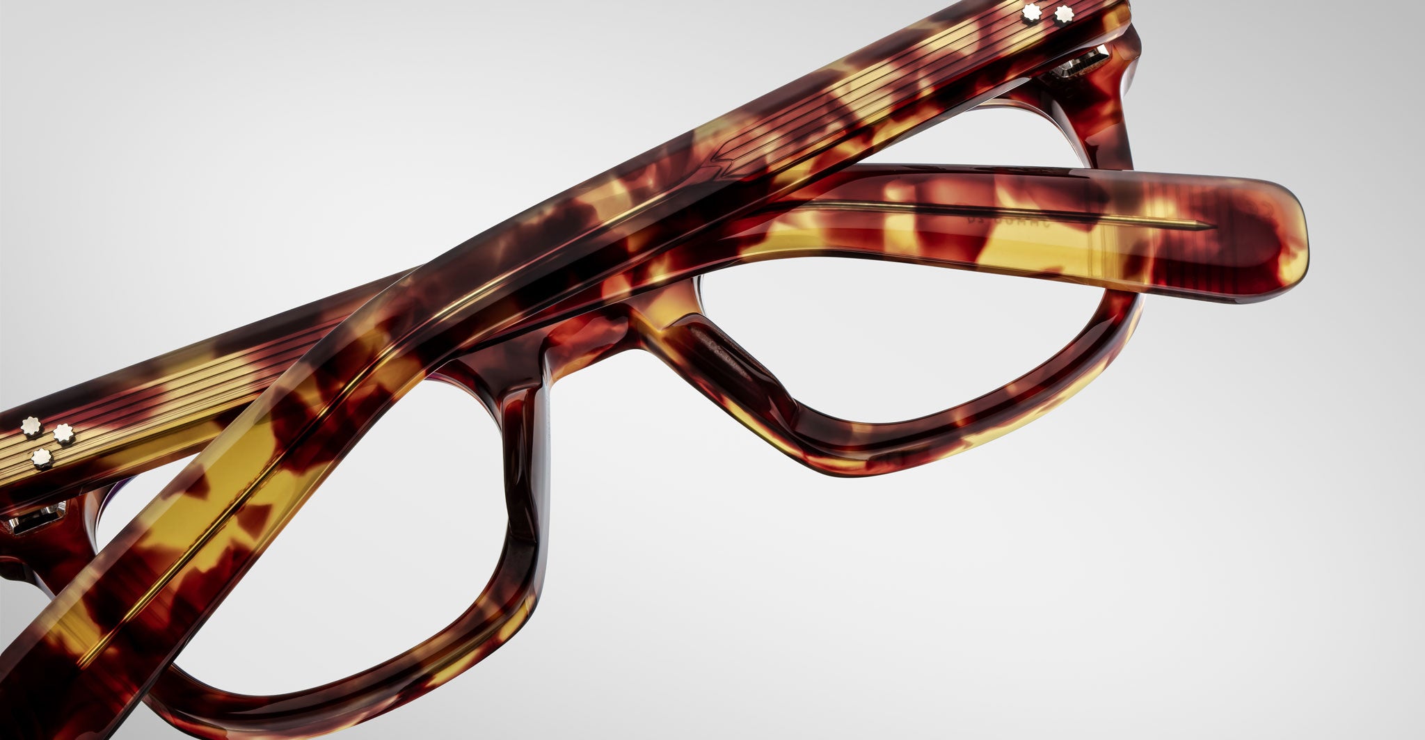 Close-up of two pairs of Jacques Marie Mage Godard tortoiseshell eyeglasses stacked together on a plain white background.