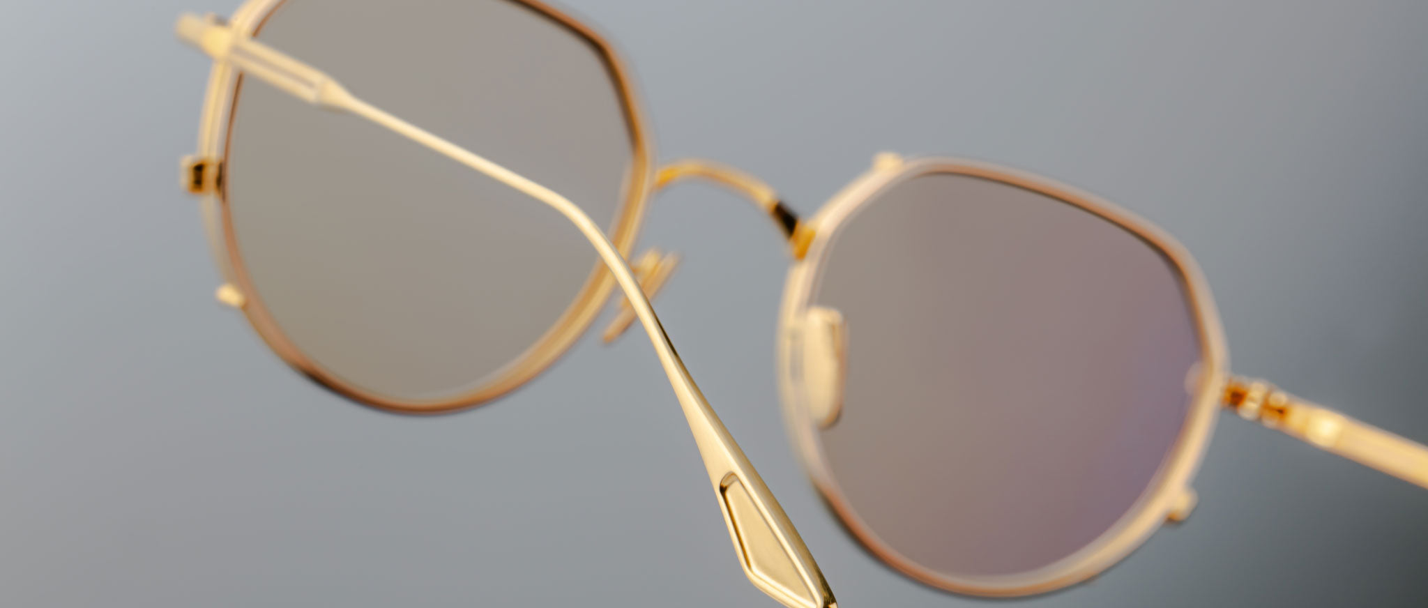 Close-up of Jacques Marie Mage Hartana eyeglasses featuring a gold geometric frame and light-tinted lenses, showcased at an angle that accentuates the thin metal construction against a softly blurred background.